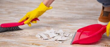 Faceless person clean up a broken plate with broom and dustpan.