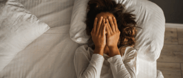 A woman. lying in bed covering her face.