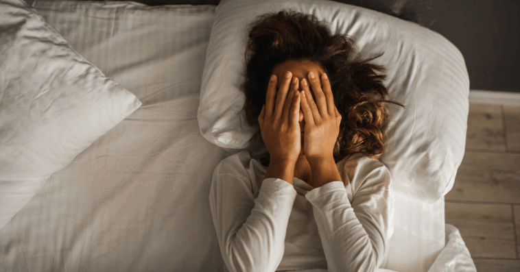 A woman. lying in bed covering her face.