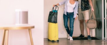 Full length pic of a couple with luggage looking around in an apartment while standing at doorway.