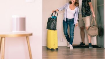 Full length pic of a couple with luggage looking around in an apartment while standing at doorway.