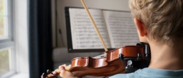 Back shot of boy practicing violin with sheet music at home.