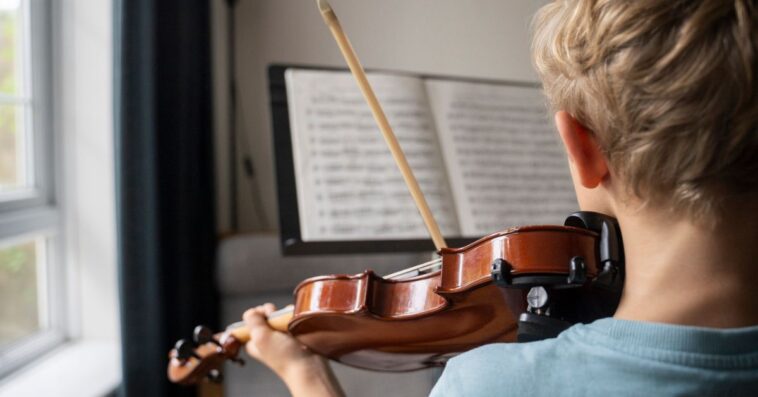 Back shot of boy practicing violin with sheet music at home.