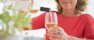 Smiling woman pouring glass of white wine.