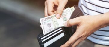 A young man holding an open wallet and counting cash.