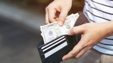 A young man holding an open wallet and counting cash.