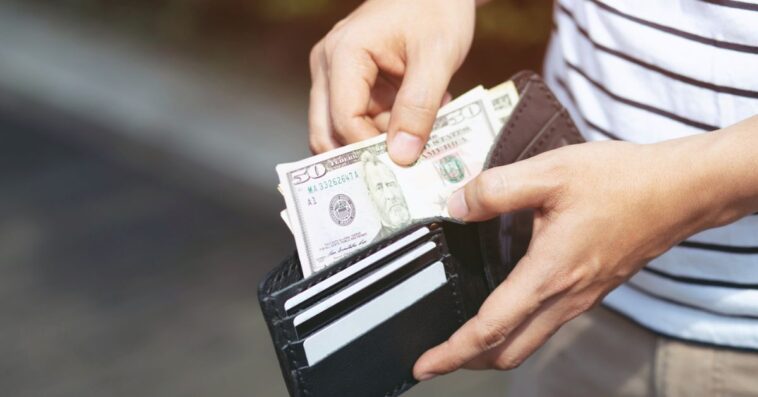 A young man holding an open wallet and counting cash.
