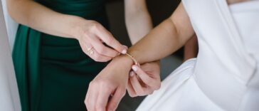 Bridesmaid in a dark green dress helps gorgeous bride to dress up and get ready for her wedding ceremony.