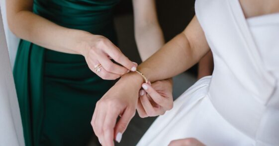 Bridesmaid in a dark green dress helps gorgeous bride to dress up and get ready for her wedding ceremony.