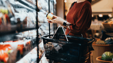 A woman looking at a jar in an aisle in the supermarket.