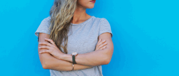 A woman with her arms crossed against a blue background.