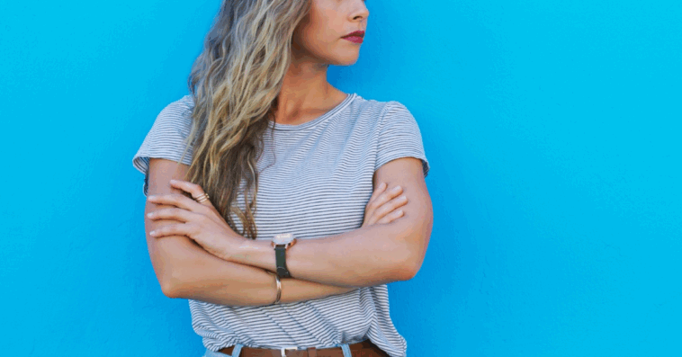 A woman with her arms crossed against a blue background.