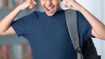 Teenager boy carrying bag in library, has his fingers in his ears.