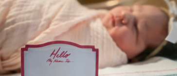 A baby in a hospital crib with a "hello my name is" sticker on it.