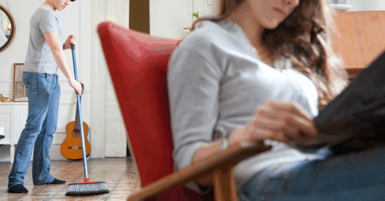 man sweeping in background as woman sits reading