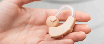 A person holding a hearing aid in their open palm.