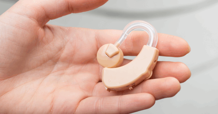 A person holding a hearing aid in their open palm.