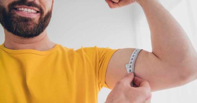 Photo of a nice, strong, young, athletic, bearded man measuring his bicep size indoors.