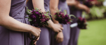 A line of bridesmaids in purple dresses holding bouquets.