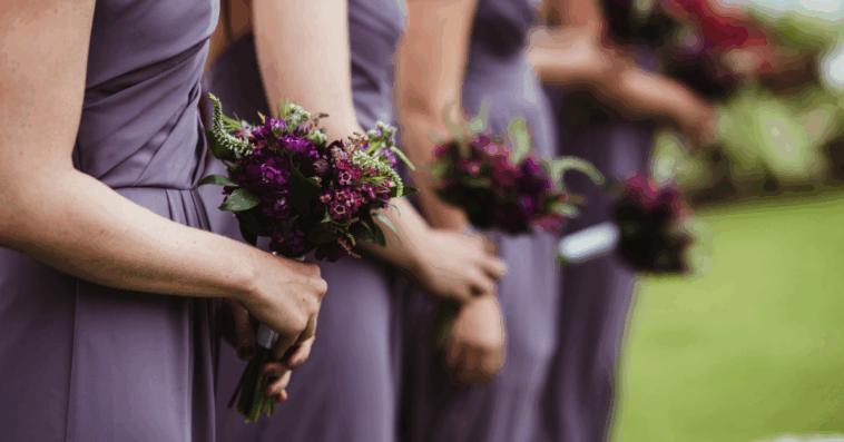 A line of bridesmaids in purple dresses holding bouquets.