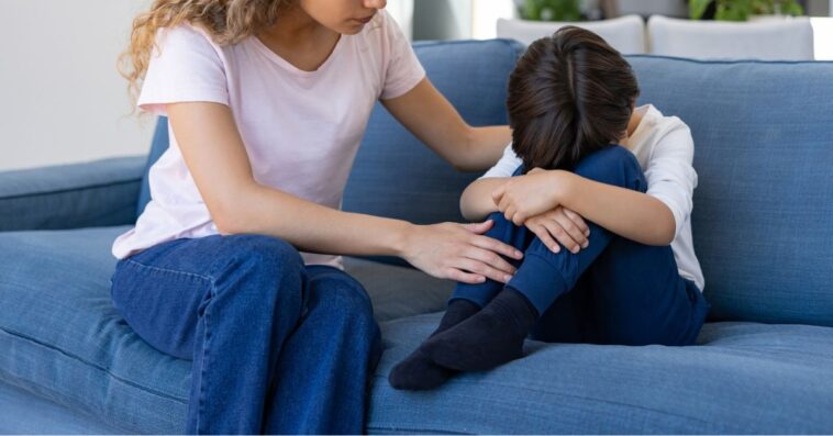Loving mother trying to calm down her sad son while he is crying at home on the couch.