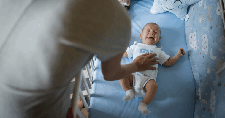 A parent leaning into a crib trying to comfort a crying baby.