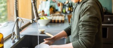 Teenage boy washing dishes in kitchen.