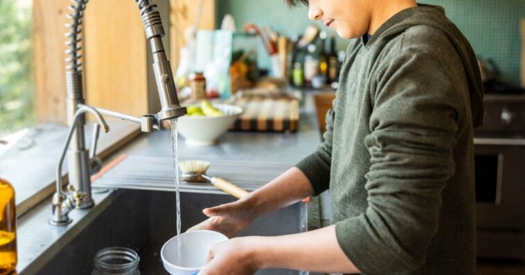 Teenage boy washing dishes in kitchen.