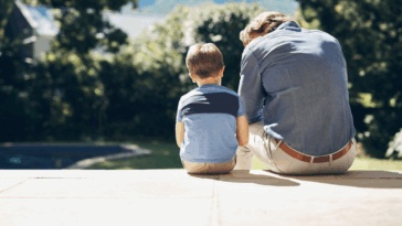 A young boy sitting next to a man looking down to him.