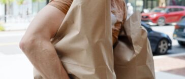 Close-up of an unrecognizable man walking down the street carrying bags of groceries.
