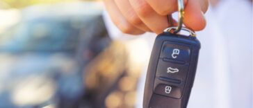 Female car salesperson handing over the new car keys. There is a new car behind her out of focus. Close up with Copy space.