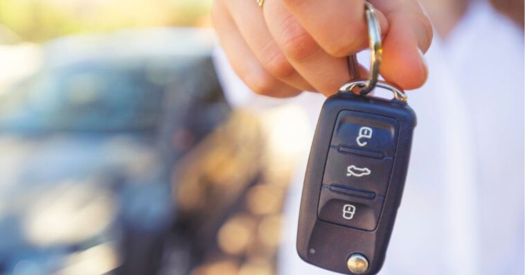 Female car salesperson handing over the new car keys. There is a new car behind her out of focus. Close up with Copy space.