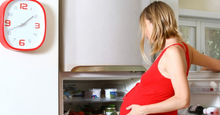 Pregnant woman with cravings looks in fridge.