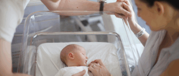 A man and a woman looking down at a baby in a hospital crib.