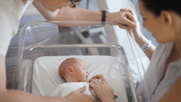 A man and a woman looking down at a baby in a hospital crib.