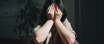 Upset teen girl sits on the floor, covering her face with her hands.