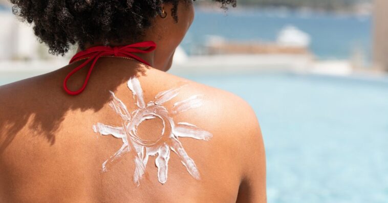 Back shot of a woman sitting on the beach with a sun made of sunscreen on her back.