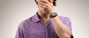 A man in a purple shirt with his hand over his mouth.