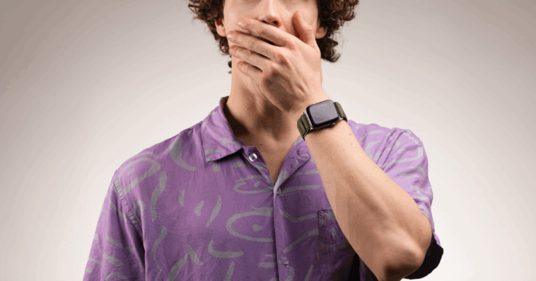 A man in a purple shirt with his hand over his mouth.