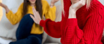 A woman pushing her hand in front of another woman sitting on the sofa.