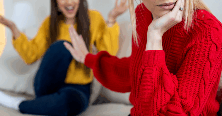 A woman pushing her hand in front of another woman sitting on the sofa.