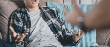 A teenage boy sitting on the couch holding out his arms and hands.