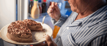 A man eating cake in front of the refrigerator.