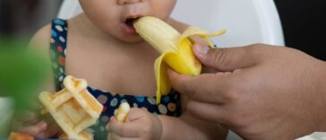 Cropped Hand Of a Mother Feeding Banana To her Daughter In a Restaurant.