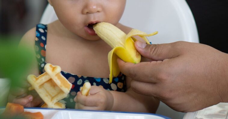 Cropped Hand Of a Mother Feeding Banana To her Daughter In a Restaurant.
