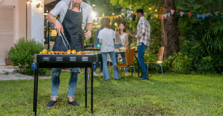person cooking on a BBQ grill as people socialize in the background