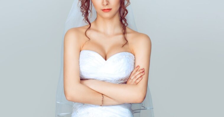 Grumpy bride. Sad and disappointed hesitating woman in wedding dress, arms folded, unhappy wife.