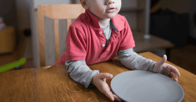 A boy sitting at a table in front of an empty plate.