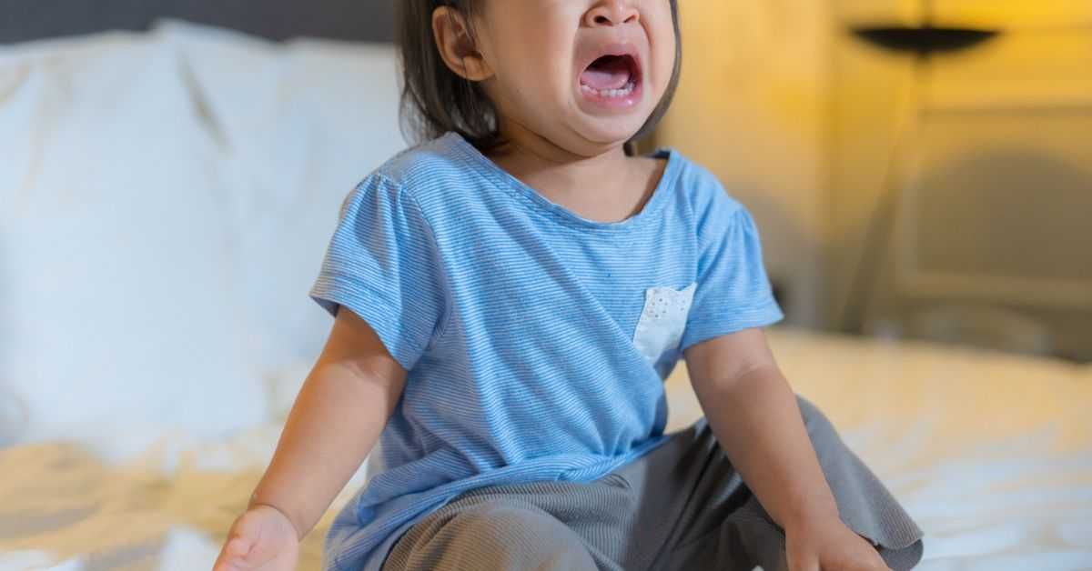 Toddler girl crying on the bed.