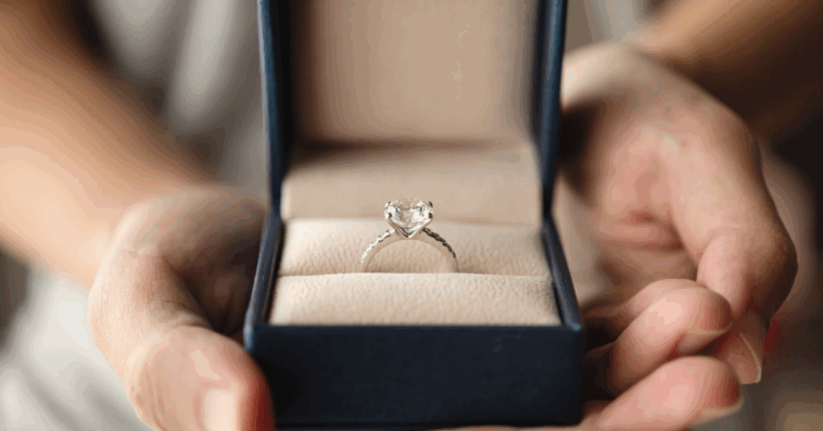 A woman holding a ring box open to reveal an engagement ring.